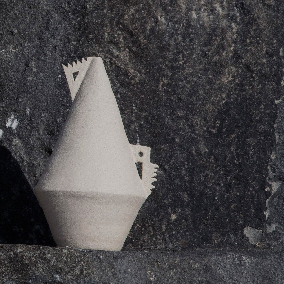 White cone shaped (soliflor) vase with details on a textured stone surface