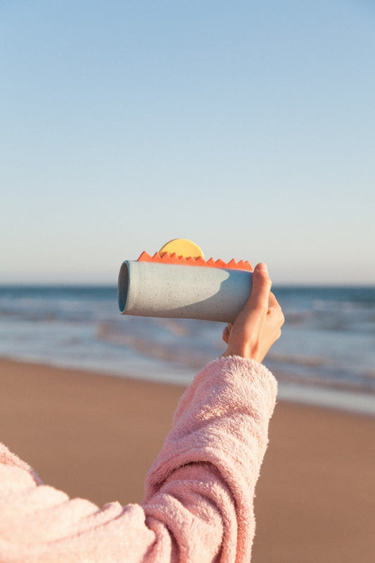 Cecile*M handmade ceramic cup held against the ocean on a sunny beach