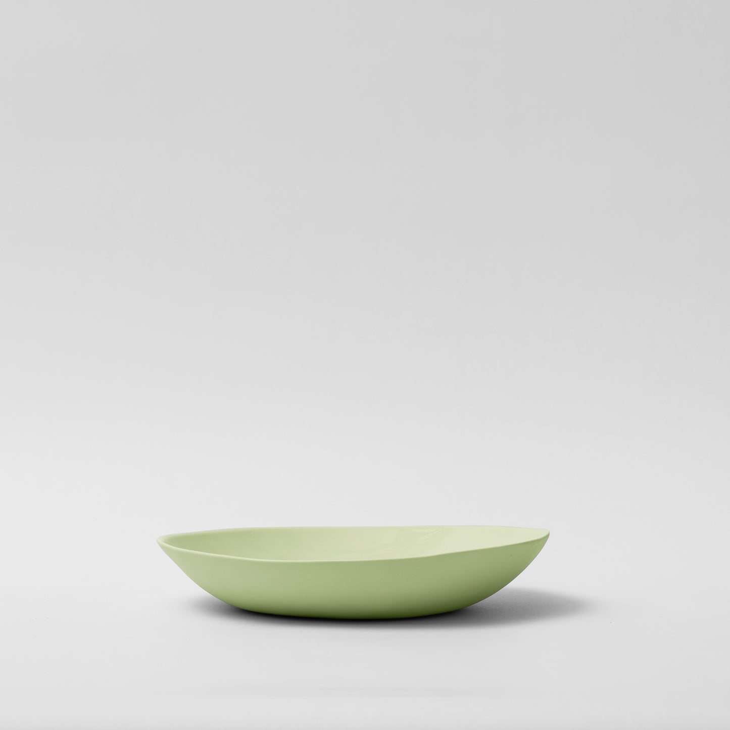 A green, irregular curved porcelain plate on a plain background.