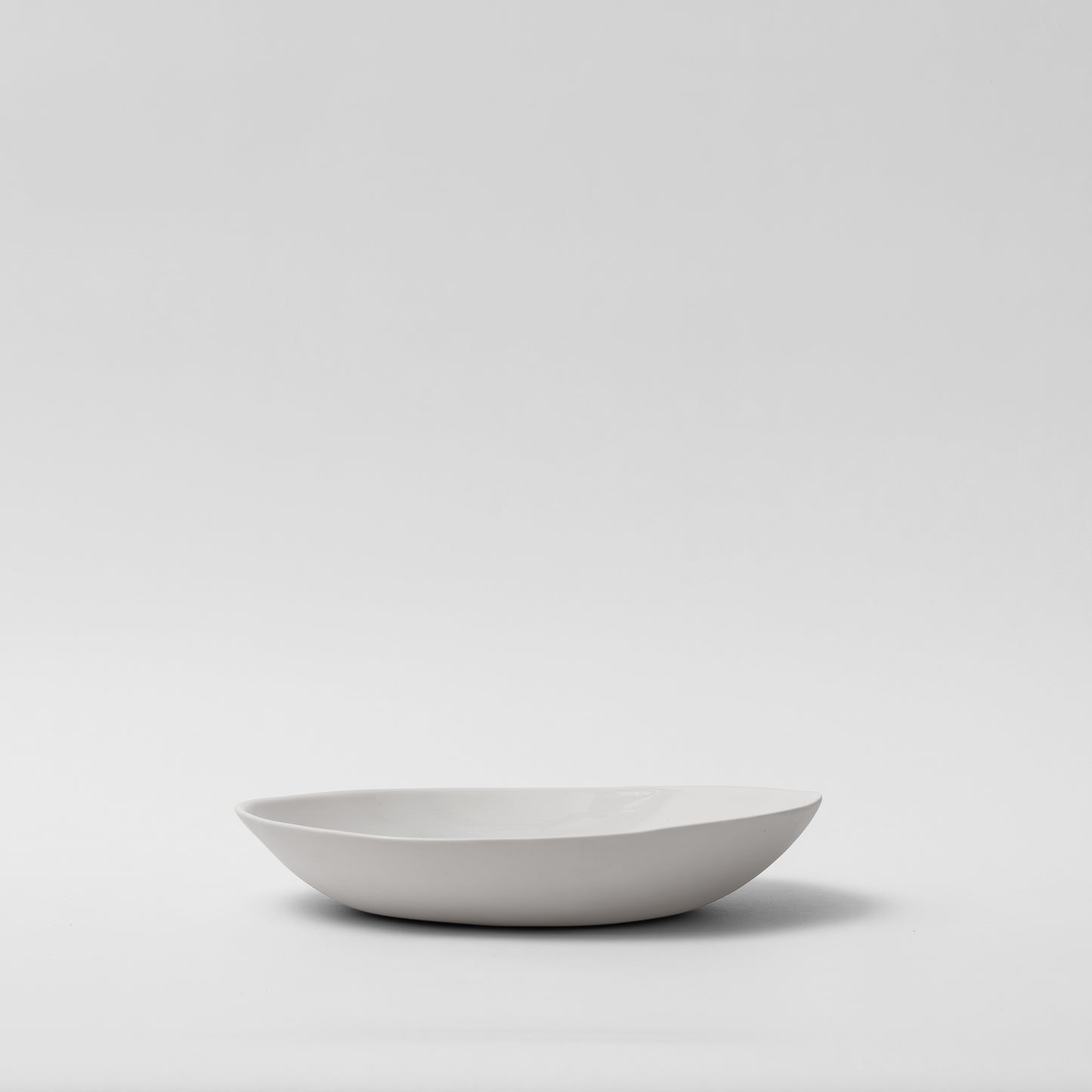 A white, irregular curved porcelain plate on a plain background.