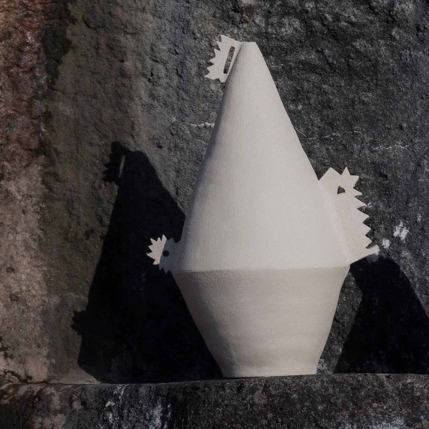 White cone shaped (soliflor) vase with details on a textured stone surface