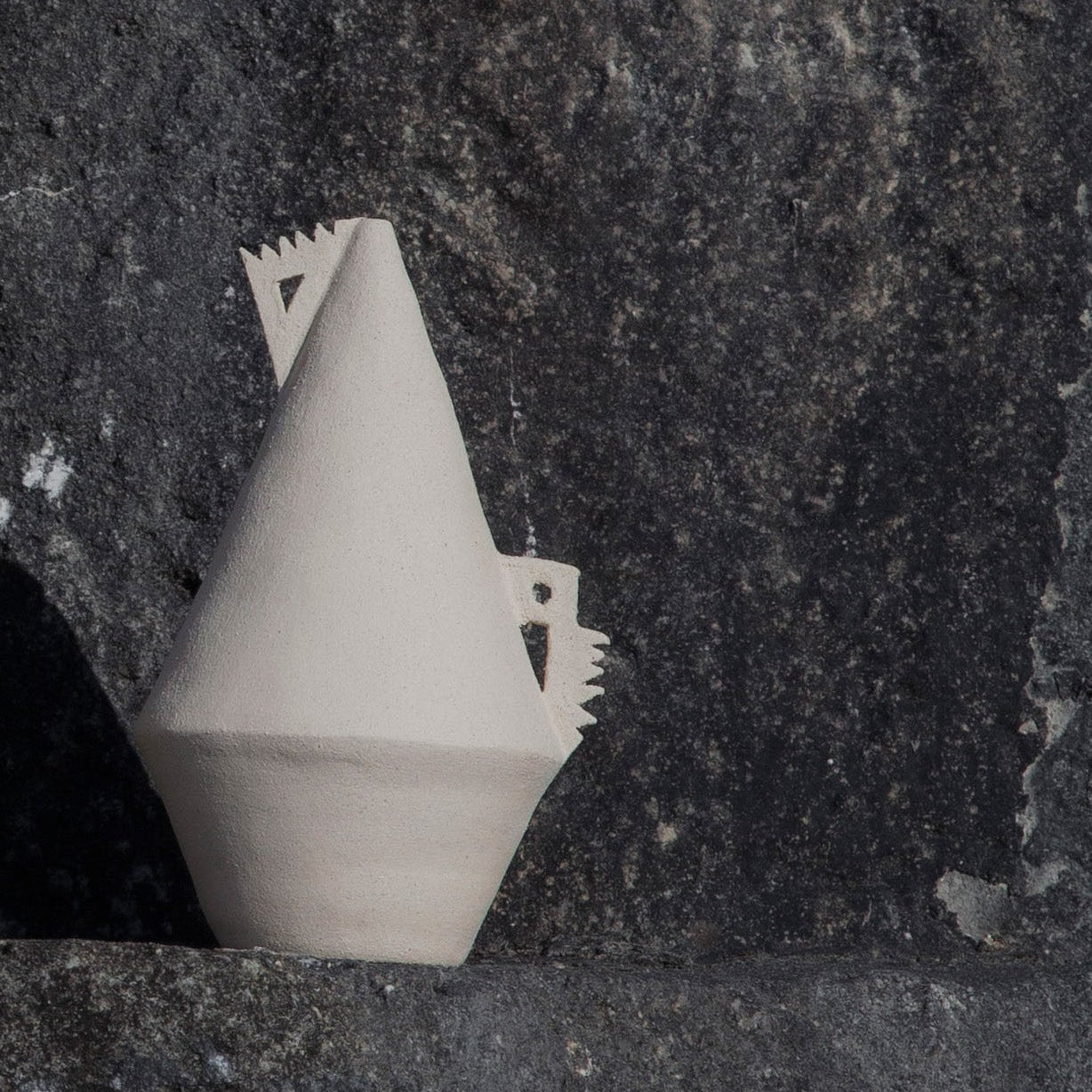 White cone shaped (soliflor) vase with details on a textured stone surface