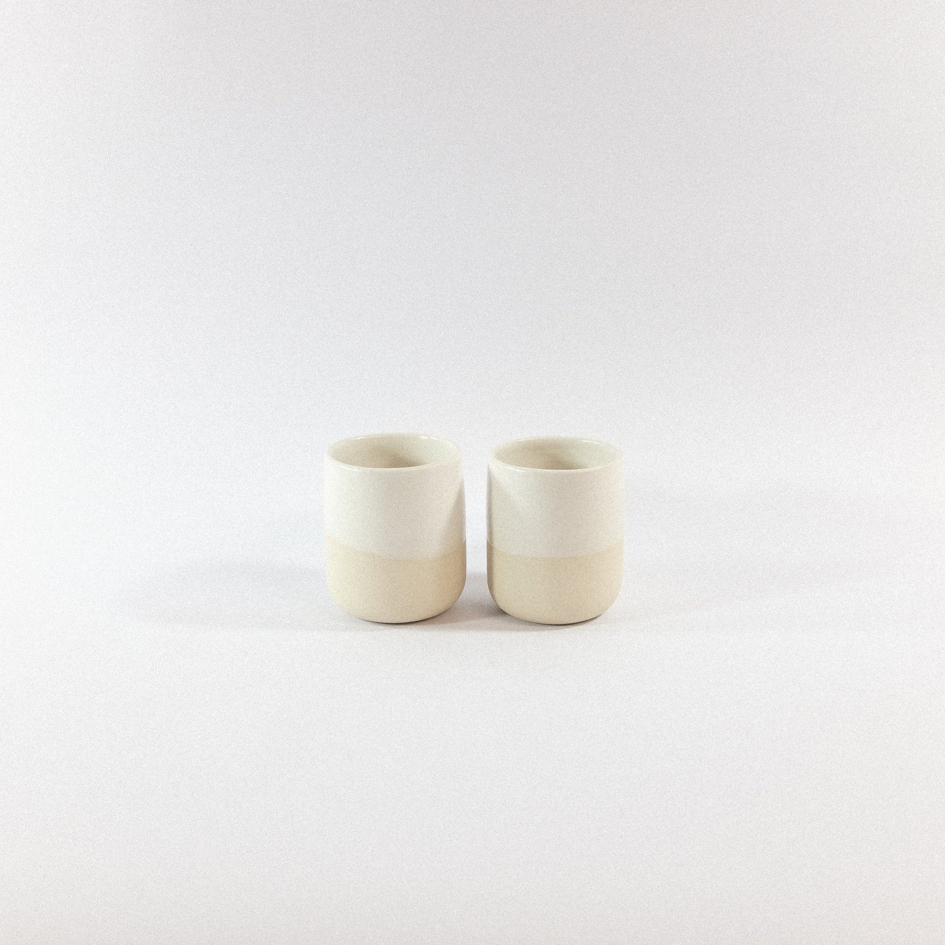 Two white stoneware tumbler ceramic cups on a white  background