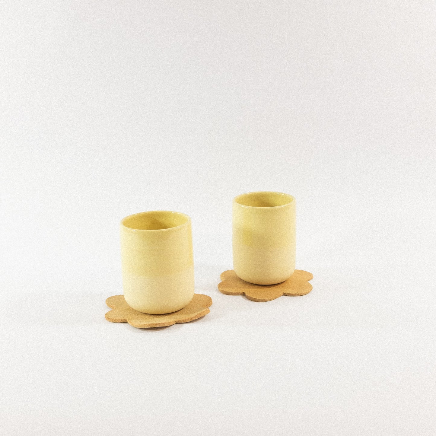 Two yellow ceramic cups with matching coasters on a white background
