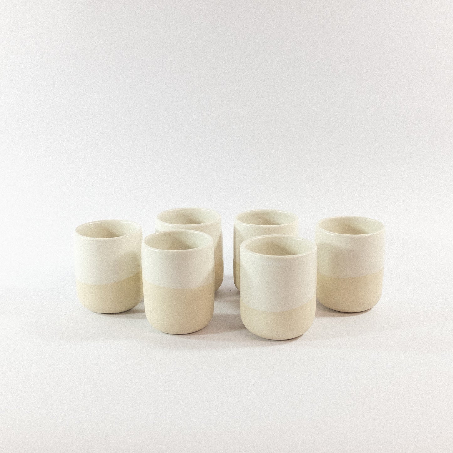 Set of six white handmade stoneware tumbler cups on a white background